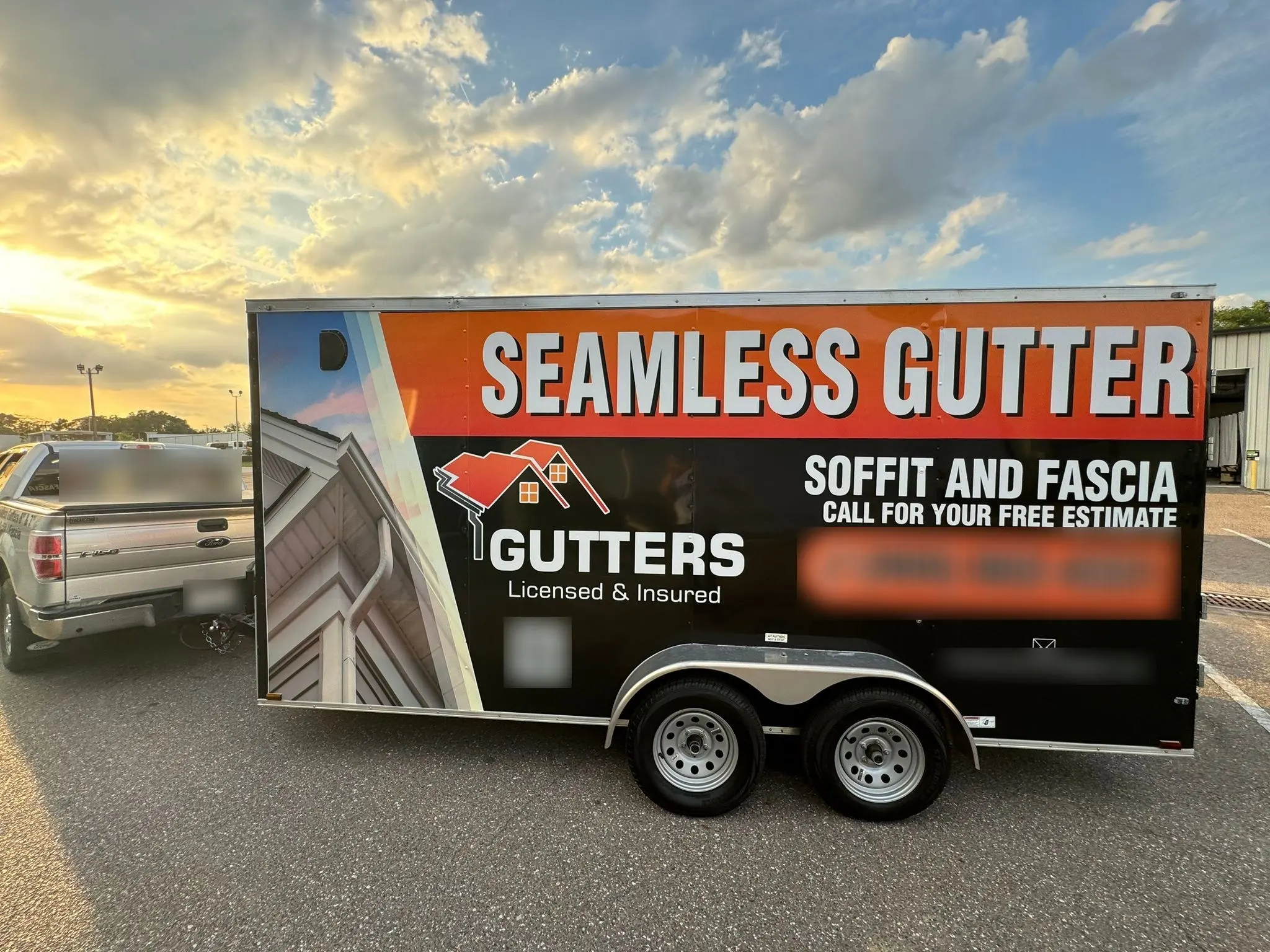 Cargo trailer wrapped in orange and black graphics, parked at sunset