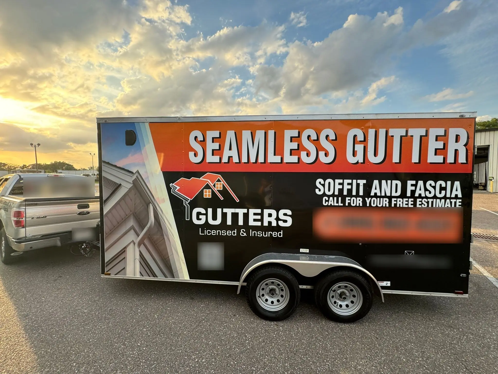Cargo trailer wrapped in orange and black graphics, parked at sunset